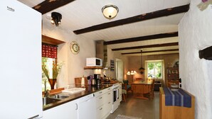 A kitchen with white cabinets, a microwave, and a sink. There is a wooden dining table with chairs and a rug on the floor. - Cozy and modern wing in Boge on Gotland's east coast | SE12011 (Slite)