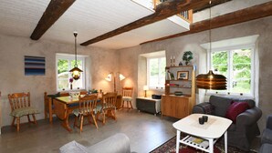 A cozy living room with a dining area, wooden furniture, and large windows. - Cozy and modern wing in Boge on Gotland's east coast | SE12011 (Slite)