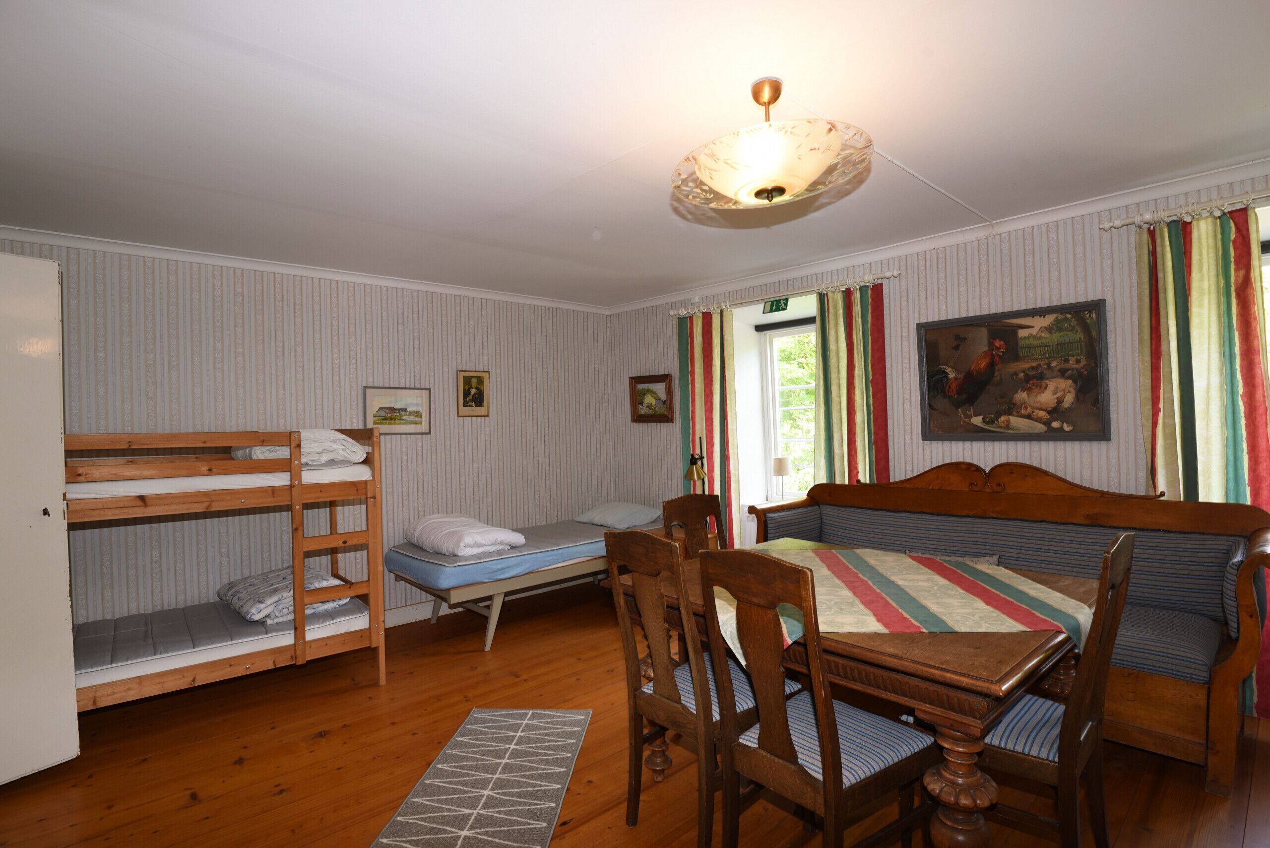Et værelse med køjesenge, et træspisebord, stole, en loftlampe og et billede på væggen.