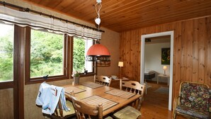 Una habitación con paneles de madera, una mesa de comedor, sillas, una lámpara colgante y vistas al exterior con vegetación.