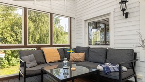 A cozy outdoor seating area with a glass table, a sofa, and a flag. - Cottage with its own sandy beach near VimmerbyI SE05018 (Vimmerby)
