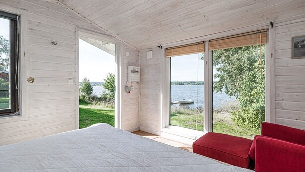 A bedroom with a large bed, a red chair, and a view of a lake. - Cottage with its own sandy beach near VimmerbyI SE05018 (Vimmerby)
