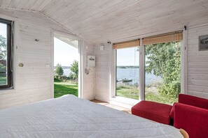 Ett sovrum med en stor säng, en röd fåtölj och utsikt över en sjö.