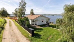A small white house with a red roof, a fenced yard, and a dirt path leading to it. - Cottage with its own sandy beach near VimmerbyI SE05018 (Vimmerby)