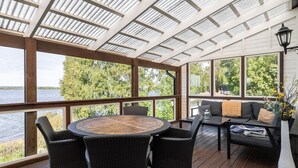A covered deck with a round table and chairs, a sofa with cushions, and a lamp. - Cottage with its own sandy beach near VimmerbyI SE05018 (Vimmerby)