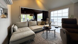 A modern living room with a sectional sofa, a round coffee table, and a view of a body of water through large windows.