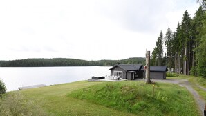 A lakeside cabin with a deck, surrounded by a forest and a clear view of the lake.