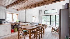 Une cuisine rustique avec des poutres en bois, un coin repas avec une table et des chaises en bois, et une grande fenêtre donnant sur un paysage verdoyant.