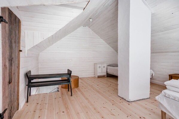 Un dormitorio tipo loft con techo inclinado, suelo de madera, un banco, un mueble blanco pequeño y una cama.