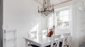 Uma área de refeições com mesa branca, cadeiras brancas, um candelabro e uma janela com vista.