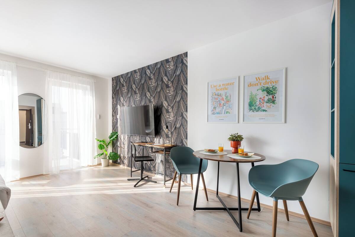 A modern living room with a dining area, a flat-screen TV, and two framed posters on the wall.