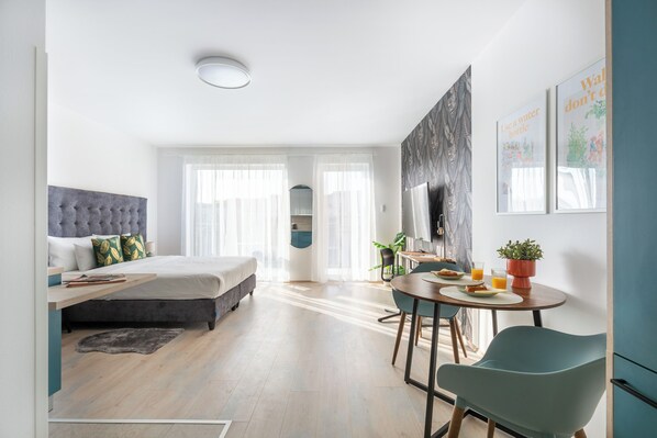 A modern hotel room with a bed, a desk, a dining area, and a large window with sheer curtains. - Hock Residence by Vagabond (Budapest)