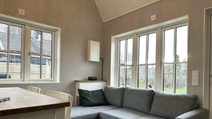 A room with a corner sofa, a dining table, and large windows.