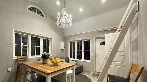 A dining area with a wooden table, chairs, a chandelier, and large windows.