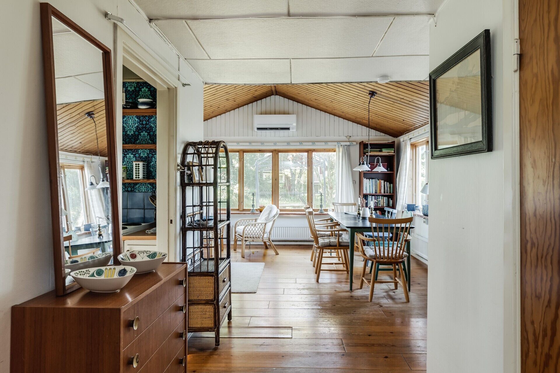 A spacious room with a high ceiling, wooden flooring, a dining area with chairs and a table, and a large window providing natural light.