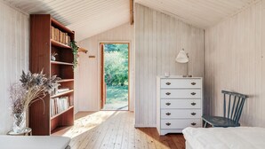 A bedroom with a wooden bookshelf, a dresser, a chair, and a window leading to a garden. - Nice holiday home near Skummelövs strand | SE02049 (Skummeslövsstrand)