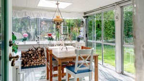 Ein Essbereich mit Holztisch und -stühlen, einer hängenden Leuchte und Blick auf einen Garten durch große Fenster.