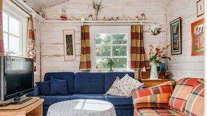 Ein gemütliches Wohnzimmer mit einem blauen Sofa, einem karierten Sofa, einem Fernseher und einem Tisch mit einer Spitzenleinentischdecke.