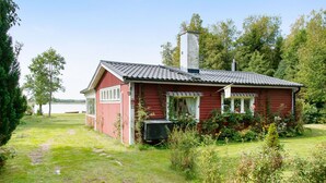 Ein rotes Holzhaus mit Schornstein, umgeben von einem grasbewachsenen Hof und Bäumen.