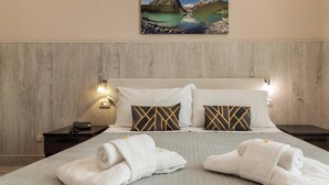 A hotel room with a bed, two pillows, a nightstand, a lamp, and a painting of a mountain landscape. - Hotiday Room Collection - Palermo Politeama (Palermo)