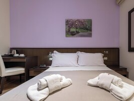A hotel room with a bed, two nightstands, a desk, a chair, and a painting on the wall.