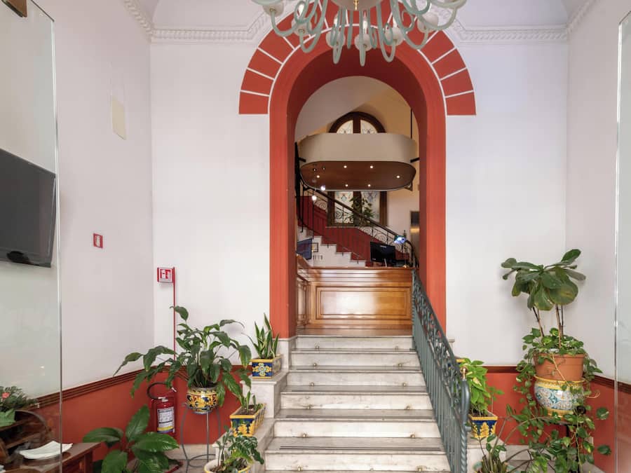 Una escalera con escalones de mármol, un arco rojo y macetas con plantas a cada lado.