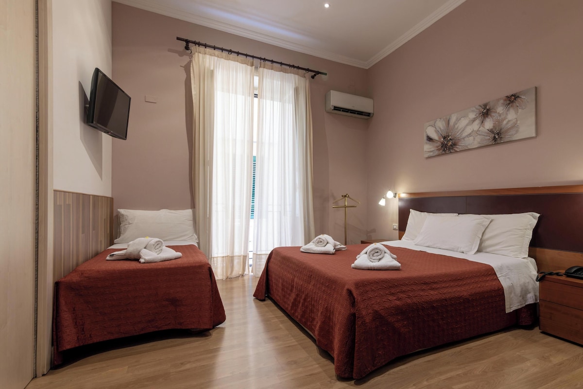 A hotel room with two beds, a TV, an air conditioning unit, and a painting on the wall.