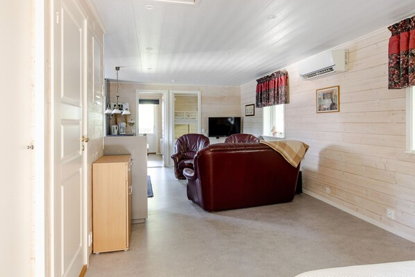 A room with a wooden floor, a sofa, a TV, and a window with curtains. - Rural apartment in Sjöared | SE02025 (Markaryd)