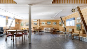 A spacious room with wooden walls and a tiled floor, featuring a dining area with tables and chairs, a sofa, and a clock on the wall. - Rural holiday home in Sjöared | SE02024 (Markaryd)