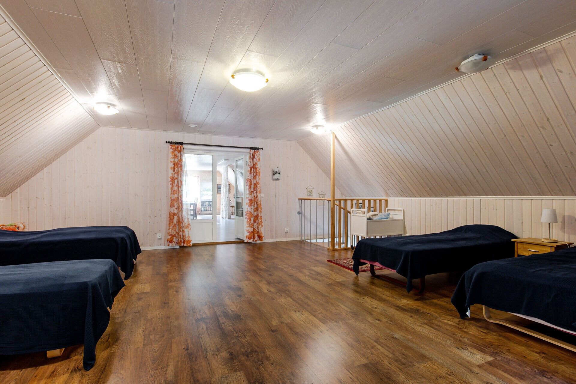 A room with two beds, wooden flooring, a sloped ceiling, and a view through a door.