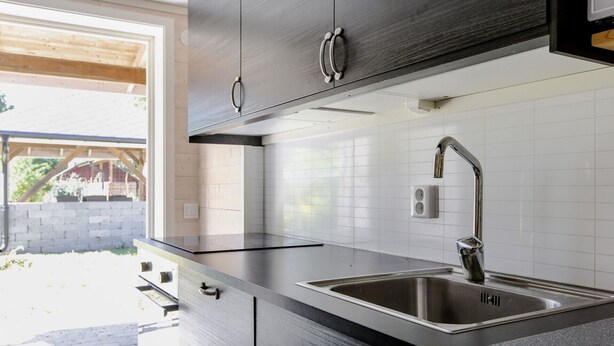 A modern kitchen with stainless steel appliances, a built-in sink, and a window overlooking a garden. - Rural holiday home in Sjöared | SE02024 (Markaryd)