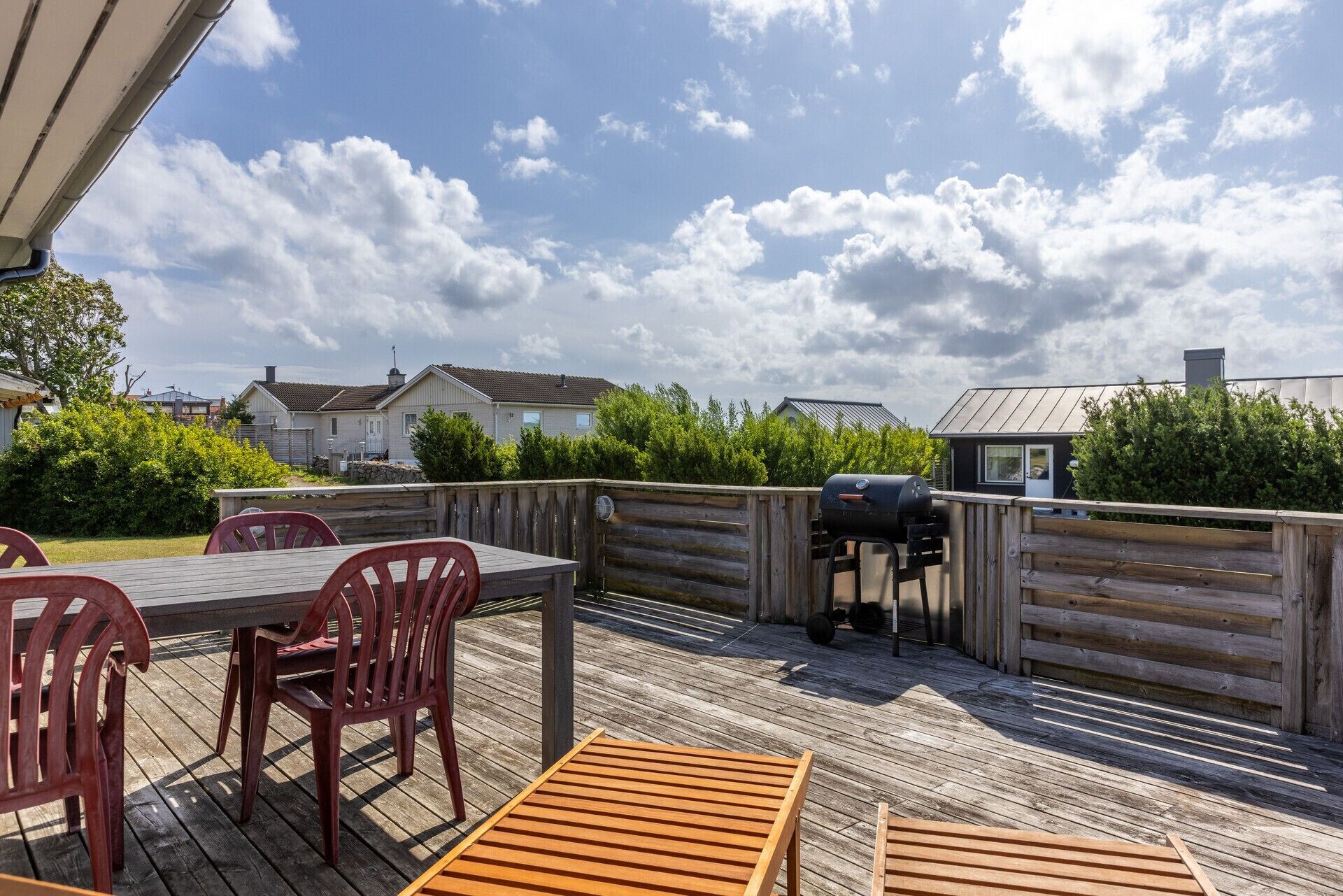 Eine Holzterrasse mit Tisch, Stühlen, einem Grill und Blick auf Häuser im Hintergrund.
