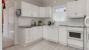 Una cocina moderna con armarios blancos, lavavajillas, estufa y ventana con cortinas.