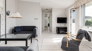 Una sala de estar moderna con un sofá, una mesa de centro de vidrio, un sillón estampado, un televisor y un ventanal grande.