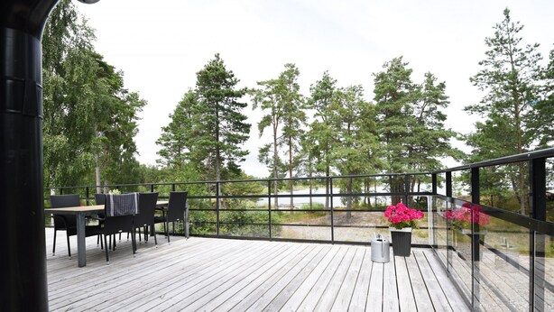 A wooden deck with a table and chairs, surrounded by glass railings and potted plants.