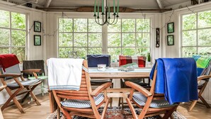 A sunroom with a wooden table, chairs, and a view of greenery through large windows.