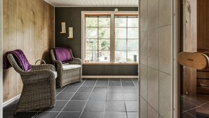 A room with a large window, two wicker chairs, a wooden door, and a tiled floor.