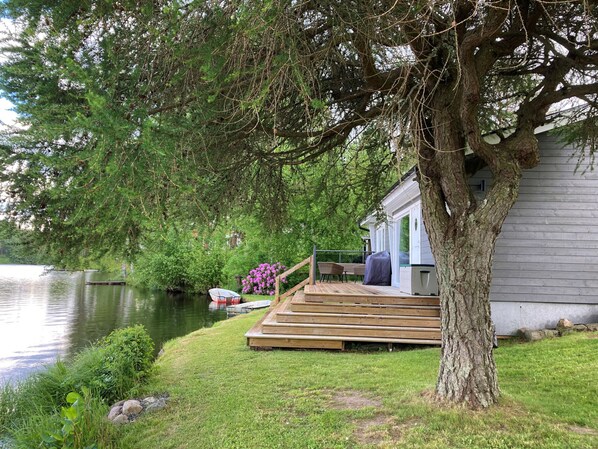 Una propiedad frente al lago con muelle, terraza de madera y una casa con zona de estar cubierta al aire libre.