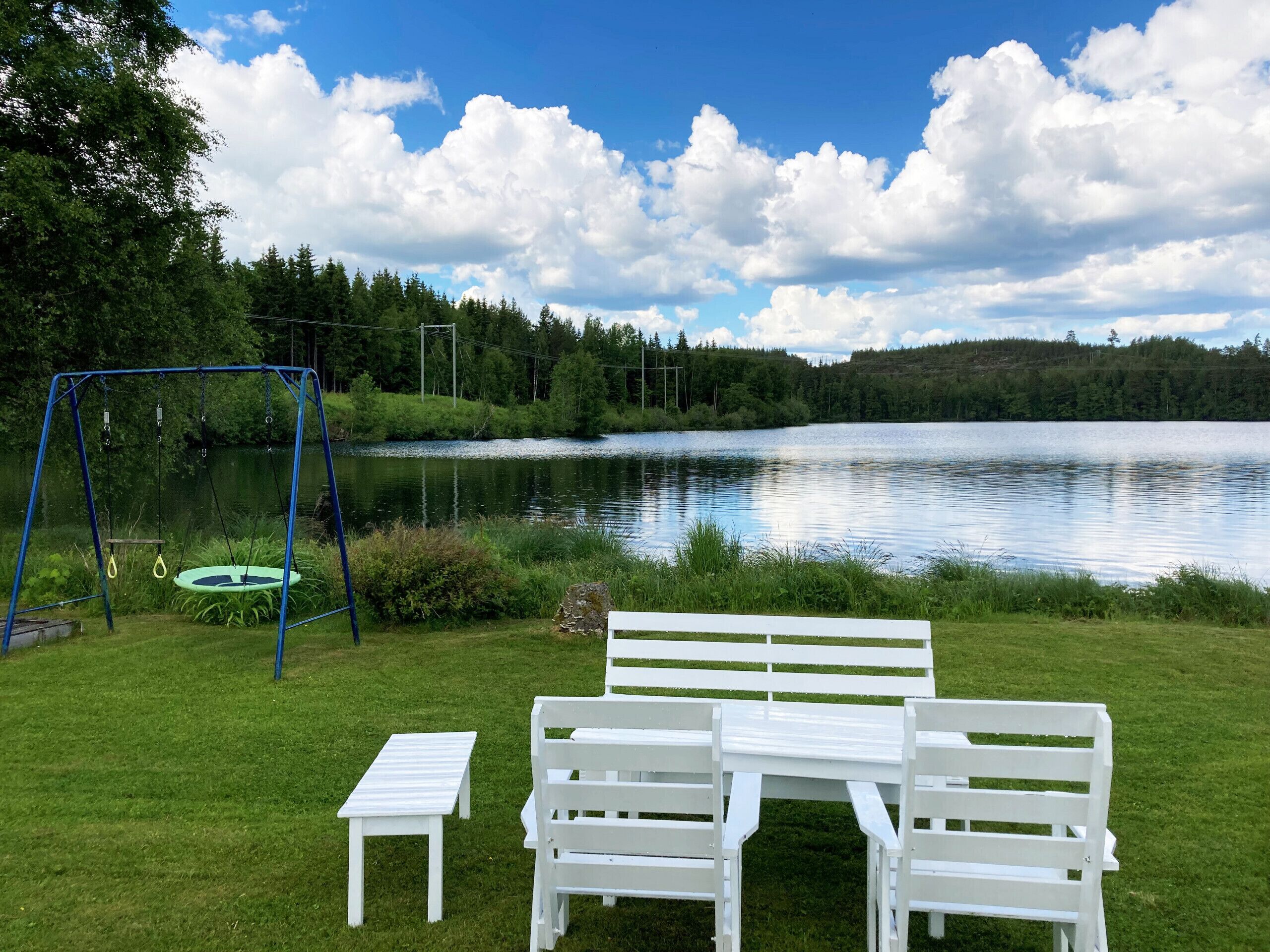 Eine Uferlandschaft mit Schaukel, Bank und kleinem Tisch.