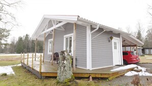 A small, single-story cabin with a porch, a door, and a vehicle parked outside.