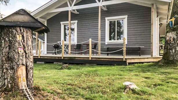 A house with a porch, a small treehouse, and a grassy yard.