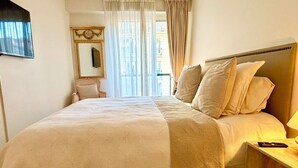A hotel room with a large bed, a nightstand, a chair, a mirror, and a window with curtains. - L'appartement Nicolo (Paris)