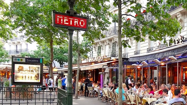An outdoor café area with tables and chairs, a metro sign, and a building with a sign reading "Le Malakoff". - L'appartement Nicolo (Paris)