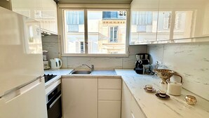 A compact kitchen with white cabinetry, a built-in oven, a sink, and a window overlooking a building. - L'appartement Nicolo (Paris)