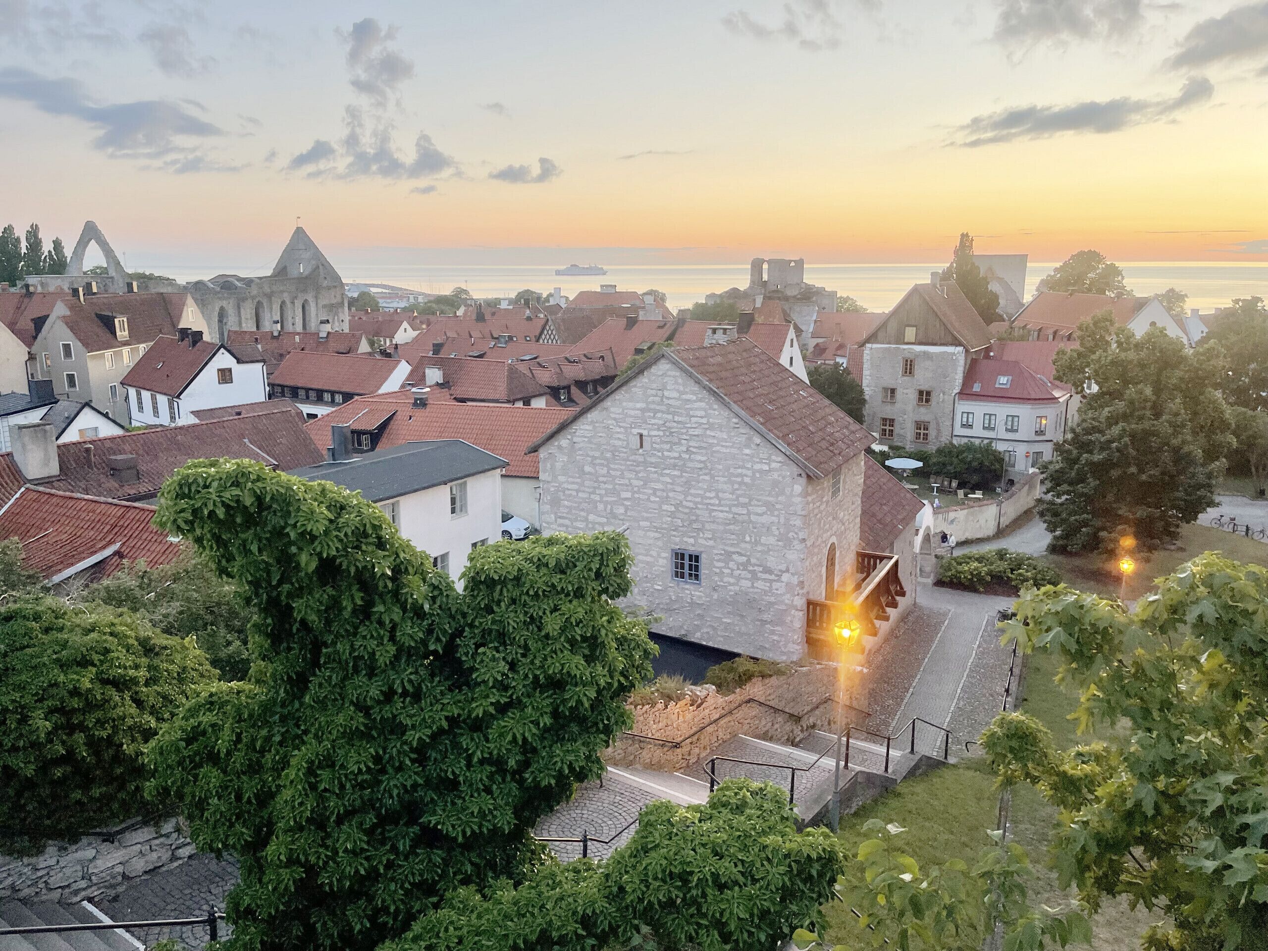 Uma cidade com edifícios históricos de pedra, uma igreja imponente e vista para o mar ao pôr do sol.