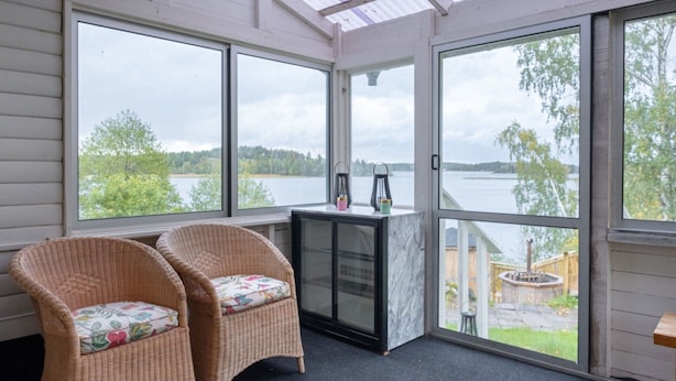A room with two wicker chairs, a marble fireplace, and large windows overlooking a lake.