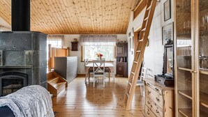 A cozy cabin interior with a wooden ceiling, a fireplace, a dining area, and a loft space with a ladder.