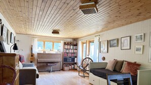A cozy room with a wooden ceiling, a desk with a chair, a bookshelf, a rocking chair, and a bed.