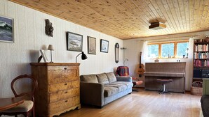 A cozy living room with a wooden ceiling, a sofa, a wooden cabinet, a guitar, and a bookshelf.