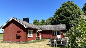 A red barn with a white door and window, a chimney, and a small porch with a table and chairs.
